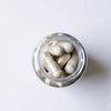 Kleen Sleep 2.0 Bottle Supplement Capsules. Top-down view of a clear glass jar filled with off-white capsules on a plain white background