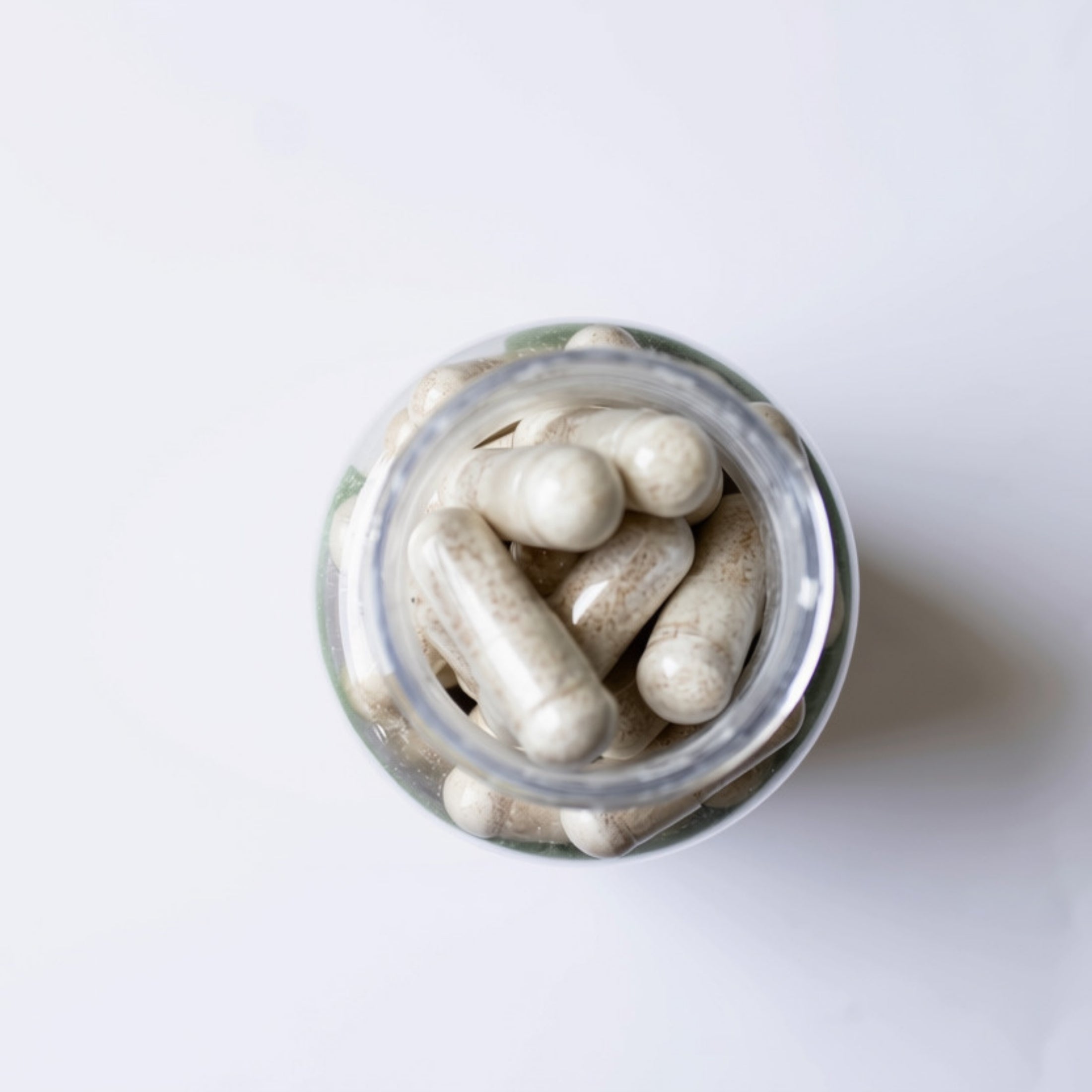 Kleen Sleep 2.0 Bottle Supplement Capsules. Top-down view of a clear glass jar filled with off-white capsules on a plain white background