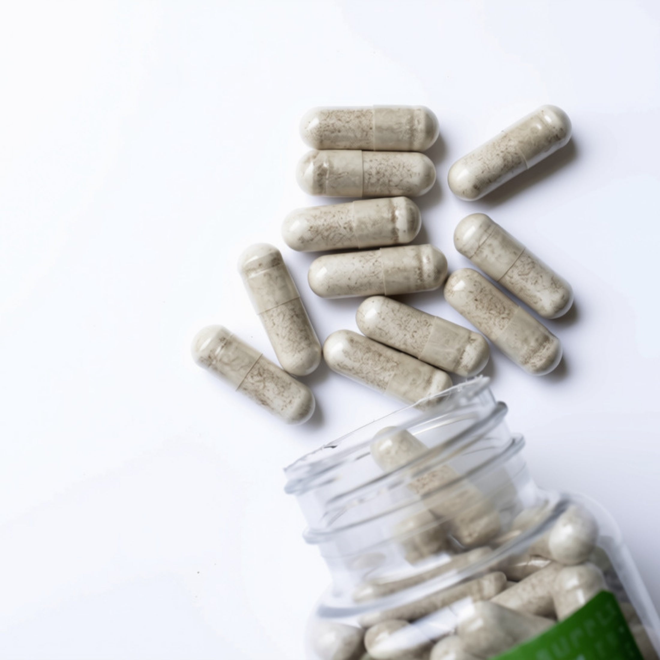 Beige herbal supplement capsules spilling from a clear plastic bottle on a white background.